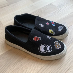 Slip-on skor från Zara - Svarta slip-on skor i storlek 38 med olika ”patches”. Bra skick. Använt försiktigt.