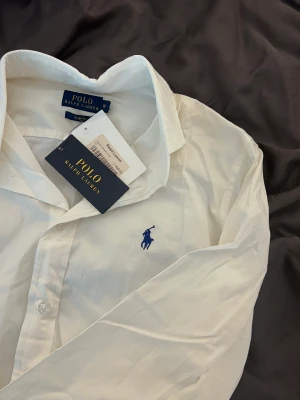 Ralph Lauren Skjorta (dam) - Säljer denna fina Ralph Lauren skjorta i modellen slim fit. Nyskick och aldrig använd. Nypris 1099kr. Säljer även en polo tröja från Ralph Lauren. 