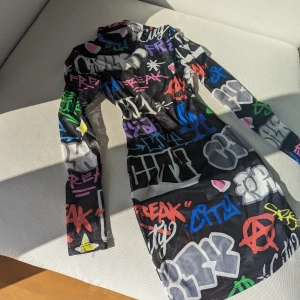 Sheer Klänning - Cool klänning med massa grafitti på i väldigt bra skick, knappt använd. OBS tyget är lite genomskinlig! Den är även ganska stretchig så den passar nog ett S också.