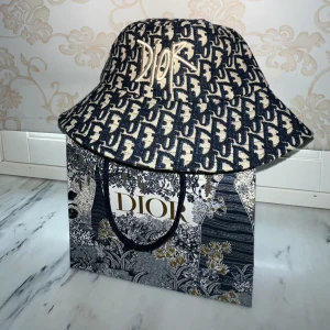Dior Hatt - Den här beige-svarta Dior-hatten är en fantastisk accessoar som kommer att lyfta din stil till en ny nivå. Hatten är helt oanvänd och har fortfarande sin ursprungliga tagg kvar, vilket garanterar dess autenticitet och kvalitet. 