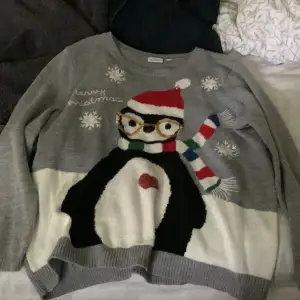 En grå jättefin jultröja med en pingvin på med tomteluva osv. Snöflingor och texten ”merry christmas”. Storlek L.