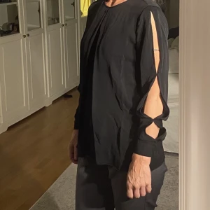 Blus Michael Kors - Svart blus med flera detaljer som ger en festlig look. Cutouts i på ovansidan av båda armarna samt detaljer framtill. 