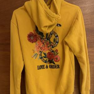 En gul/orange jätte fin hoodie med text ”love and order” och som har ett coolt tryck på ryggen!
