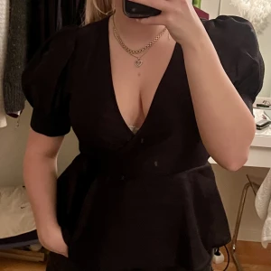 Svart blus med puffärmar  - En svart blus med djup urringning som även har puffärmar. Man knyter tröjan i sidan av den och gör en liten rosett. 