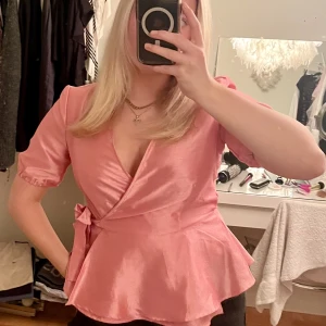 Jättesöt rosa blus  - En jättesöt rosa blus med knytning och väldigt lätta volanger längst ner. Passar till vardags och fest. 