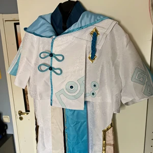 Genshin Impact Chongyun Cosplay - XL, ej asiatisk storlek! Ej använd. Originalpris 1300kr. Längd på overall: 129cm. Bred - byst: 49cm. Bred - höften: 55cm. Axelbredd på hoodie: 47cm. Kardborreband på bältet. 