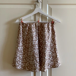 Beige kjol med vita blommor - Gullig beige kjol med vita blommor.🌷Den sitter väldigt fint och passar perfekt till en söt topp nu på sommaren. Hör av dig vid frågor eller funderingar. Ta hand om dig!💌 