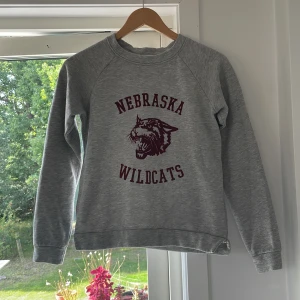 Grå tröja - Grå hoddie med röd text på. Den röda färgen är tydligare i verkligheten. En jätte fin tröja som passar perfekt till hösten. Varm, skön bomull och färger som är  lätta att matcha till. Har varit väldigt älskad men är fortfarande i jätte fin kvalite.