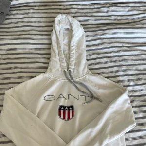 GANT - Hoodie - Vit GANT-hoodie i storlek S. Det finns en fläck på slutet av tröjan, har inte testat få bort den men det går säkert bort med fläckborttagning! Den är liten i storleken, skulle säga att den passar en XS
