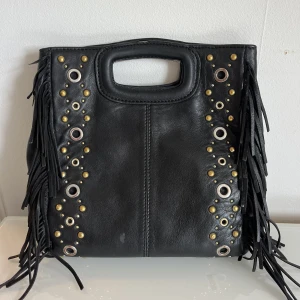 Maje väska  - Säljer denna otroligt fina Maje väska med nitar. Dust bags både till väskan och bandet. Väskan och bandet säljs tillsammans. Bandet på bilden köptes separat för 1500kr och de tunnare bandet som medföljer när man köper väskan finns med prislappen kvar.