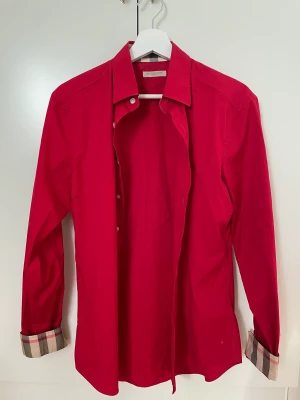 Burberry skjorta - Tja!  Säljer nu denna röda burberry  skjorta som jag köpte på plick för ett tag sedan, skjortan har inga defekter eller skador och är i top notch skick. Obs! Inget äkthetsbevis, endast mitt ord på det. Säljer denna nu för 1000kr Kontakta kring frågor! 