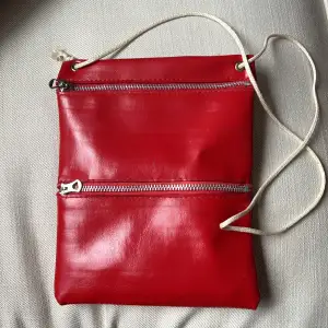 Röd väska. 14 x 18 cm. Lång rem. Frakt spårbart (29 kr) eller post (18 kr).