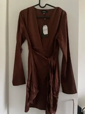 En brun oanvänd silkesklänning från Asos. Sitter väldigt fint runt kroppen och ett snöra där du kan reglera hur tajt den ska sitta vid midjan! 🤎