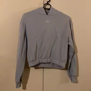 Ljusblå hoodie med nyc text - Säljer denna snygga, ljusblåa, lite croppad hoodie med vit nyc text från h&m då den inte kommer till användning. Använd fåtal gånger och är i bra skick! 💙