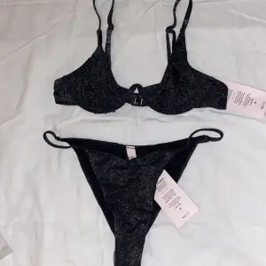 En svart glittrig bikini från Nelly. Helt ny. Storlek överdel: 70A. Storlek underdel: XS. Kan köpas var för sig. Priset kan diskuteras. Orginalpris överdel: 259kr. Orginalpris underdel: 159kr. Säljer över: 180kr, under: 80kr 