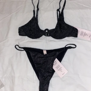 Nelly Glitterbikini - Säljer över: 100kr, under: 50kr. En svart glittrig bikini från Nelly. Helt ny. Storlek överdel: 70A. Storlek underdel: XS. Kan köpas var för sig. Priset kan diskuteras. Orginalpris överdel: 259kr. Orginalpris underdel: 159kr. 