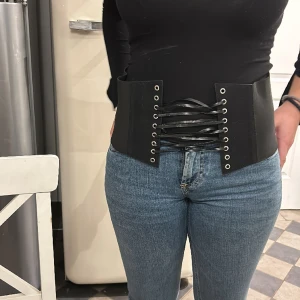 Korsett/skärp i stretch  - Svart korsett/skärpfrån Bik Bok i stretchigt material med tre tryckknappar bak. Kan regleras och dras åt fram så som det passar. One size.