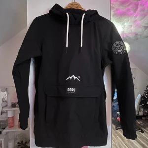 Svart dope hoodie  - Säljer denna svarta dope hoodie då den inte används mera. Den är sparsamt använd under 1 säsong och har inga defekter.   Den har en ficka vid armen för liftkort samt en ficka framtill.    Den är inte fodrad men vattentät.  Den är i storlek xs.