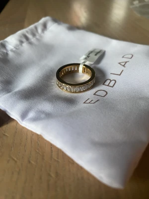 Edblad guldring  - Edblad Radiant Ring Gold. 14 karat guldpläterat ring. Helt oanvänd. Lappen sitter kvar på och dustbagen finns kvar. Köptes för ca en månad sedan men inte använts. Storlek 8 (17,5 mm) Nypris 499 kr