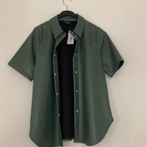 Skjorta - En grön/turkos kortärmadskjorta i skinn material. Från Gina i stl S aldrig använd