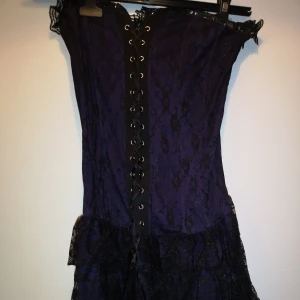 Lila Klänning burleska - En jättefin korsettklänning i svart och mörklila. Den har ett litet hål i sidan, men det går att laga för den händiga. Se bild 3