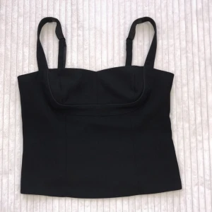 Svart topp - Korsettliknande svart topp. Står ingen storlek men skulle definitivt säga att den motsvarar en L. Superfint skick, inga anmärkningar. 
