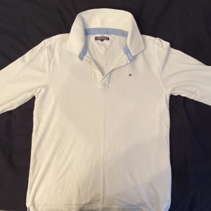 Tommy Hilfiger långärmad piké - Vit stilig längärmad Tommy Hilfiger piké som inte används längre. Storlek 164. Säljs i befintligt skick