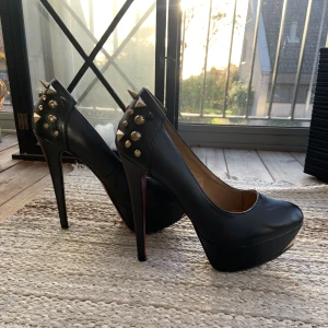 Klackar - Svart röda klackskor med guldiga nitar, slitna på undersidan. Höjd: 13,5 cm Plattformen: 3,5 cm 