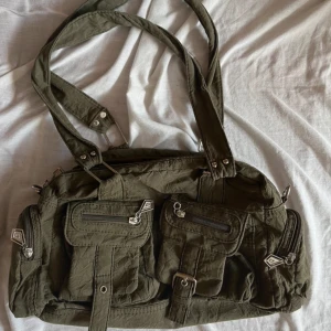 Fin grön khaki väska - Jätte fin väska, det är några defekter på den, trasig dragkedja inuti och ena knappen på fickorna på framsidan är sönder, jag köpte den second hand för 400 kr och den var redan sönder då🫶om man stryker den blir den bättre, skriv om ni vill ha fler bilder
