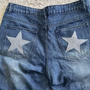 Jeans med stjärnor  - Mörkblåa Jeans med stjärnor sydda på bakfickorna. Jeansen är köpta secondhand och stjärnorna är påsydda (i jeansmaterial) av mig. Byxorna är low rise och i jättefint skick.