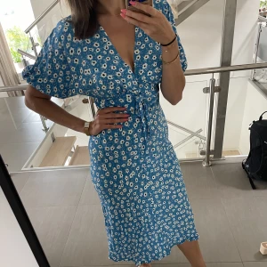 Blå, blommig sommarklänning - Fin blommig sommarklänning perfekt till midsommaren! Använd en gång i fjol. Köpt från ASOS, storlek 38. Normal i storleken. Klänningen är midi längd och är gjord i bommol.