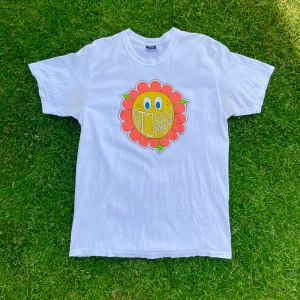 Stüssy t-shirt  - Vit Stüssy t-shirt med tryckt blomma på. Inköpt på NK Stockholm. Strolket large och gjord i mexico i 100% bomull. Tröjan har gulnat något i armhålan, går att ta bort med bikarbonat.