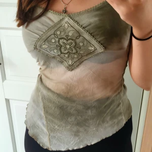 Topp - Asymmetrisk topp, seetrough vid midjan men täckande vid brösten, fina detaljer så som spets och "medaljonger" vid axlarna. Står ingen storlek men tyget är stretchigt så passar nog de flesta.