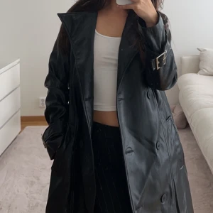 Trenchcoat i läderimitation - Aldrig använd! Medföljer bälte/band. Lite oversize