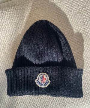Moncler mössa - svart - Svart moncler mössa. Knappt använd! Kan säkert hitta kvitto om så önskas. Helt ny. Köpt för 2 år sedan men använd kanske 3 gånger! Nypris ca 2400kr