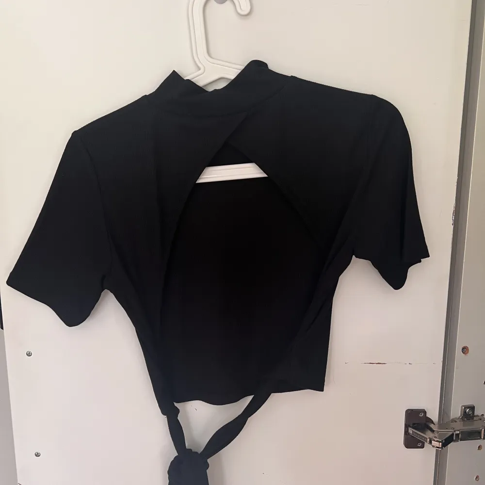 En svart t-shirt med öppen rygg,  knytning längst ner och hög krage. Använd ett fåtal gånger. Storlek M. Från NA-KD. T-shirts.