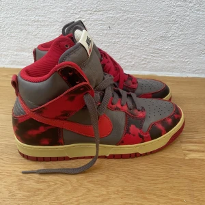 Nike Dunk High - Röda och svarta tie dye/camo mönster. Bara använda ett fåtal gånger, säljer eftersom de är för små. I mycket bra skick, nästan som nya. Levereras med extra skosnören i rött och grått (bild 3). Nypris: ca 2000 kr