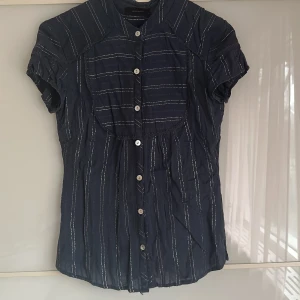 Silver blå  - En liten blus i marinblått med silver detaljer och snäckknappar. S men även xs kan ha den. 