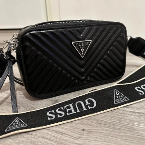 Guess väska / camera bag  - Väska från guess, svart PU läder. Snygg axelrem.  Silverdetaljer. Flera fack inuti.   Nyskick!  Fick i gåva men säljer den vidare.  Fin julklapp   Önskas fler bilder, skriv. 