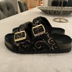 Svarta och guldiga sandaler - Ett jättefint par svarta sandaler med guld detaljer. De är i använt skick, skriv privat för mer bilder! Slitaget är inget man ser när man har på dem dock! I storlek 36, men skulle säga att de passar 37 också! Skriv privat för mer info och bilder