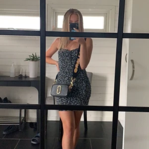 Klänning - Svart/blå, blommig, strukturerad klänning med rosett! Säljer pga av att jag inte använder plagget längre. Storlek: XXS (passar de som bär XS). Skick: Mycket bra och knappt använd.