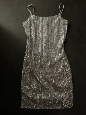 Paljettklänning - Helt ny figursydd, kortare paljettklänning. Dragkedja i ryggen. Okänt märke  Storlek: 34/XS Färg: silver glitter, ljusgrått tyg 