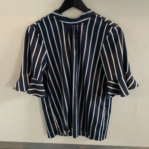 Blus från Vero Moda  - Randig blus från Vero Moda. Högre hals och ärmar med volanger. I fint skick. Storlek M