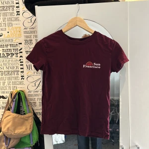 Vinröd t-shirt - Vinröd t-short från Bershka i storlek xs. Väldigt skön och har ett tryck på en soluppgång med texten ”San Francisco”