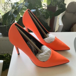 Orangea pumps  - Nya och oanvända högklackade pumps i läderimitation, perfekta att piffa upp jeans eller en svart eller vit klänning med! Färgen är mest lik bild 1-2. Klackhöjd 10cm. Extra klackar medföljer. Normala i storlek. Köpta för 369kr. 