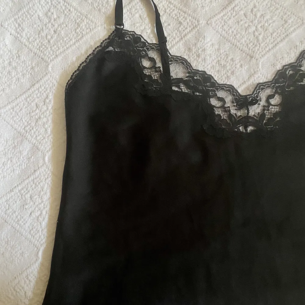 Ett svart linne i silkesaktigt tyg med fina detaljer :)  En bred spetskant och svart rosett vid urringningen & en liten spetskant längs ryggen och nedre kanten av linnet. Justerbara axelband! . Toppar.