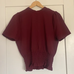 Vinröd topp - Vinröd topp med slits i ryggen med liten knapp knäppning, skrunchad i midjan, lite använd 