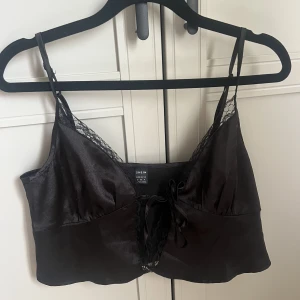 Svart satin topp - Svart topp i satin material och spets, samt knytning framtill. Kan justera axelbanden 