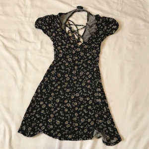 Svart blommig klänning  - - Plagg: Kläning - Mönster: Blommig (Prästkrage) - Färg: Svart - Storlek: M - Märke: Bershka - Skick: Mycket bra  - Egenskaper: Kort, Tight, öppen rygg (sträng knyt), puffärm, prästkragar Kontakta mig gärna vid frågor 💕 