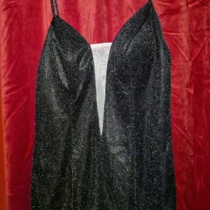 Vart glitrig kläning - Svart glitrand lång klänig med lite vit tyget i melan bröstet aldrig använd då den inte pasa mig 